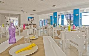 Bluu Bahari Hotel في كارباثوس: غرفة طعام مع طاولات بيضاء و مزهرية أرجوانية