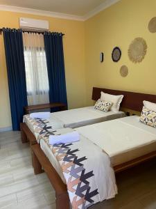 two beds in a room with blue curtains at Havana Hôtel in Morondava
