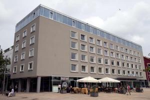 un grand bâtiment avec des tables et des parasols devant lui dans l'établissement Nordsee Hotel City, à Bremerhaven