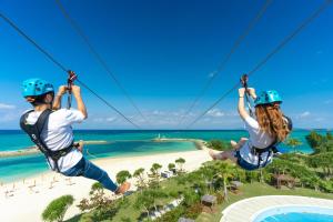 恩納的住宿－沖繩太陽碼頭喜來登度假酒店，两人在海滩上乘高空滑索