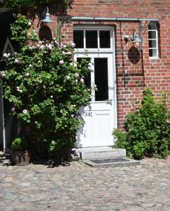 a white door on a brick building with a bush at Schrotboden in Geschendorf