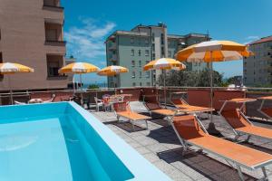 a swimming pool with chairs and tables and umbrellas at Hotel Joli in Cesenatico
