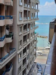 Un grand bâtiment avec des voitures garées en face de l'océan dans l'établissement شقة فندقية اسكندر ابراهيم, à Alexandrie
