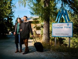 un uomo e una donna in piedi accanto a un cartello con una valigia di Alpenpark Turrach by ALPS RESORTS a Turracher Hohe