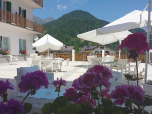 un patio con mesas, sombrillas blancas y flores púrpuras en Hotel Pineta, en Falcade