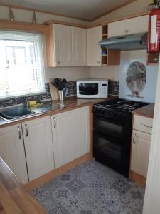 a kitchen with white cabinets and a black stove top oven at 24 The Beeches Caravan Park in Gilcrux