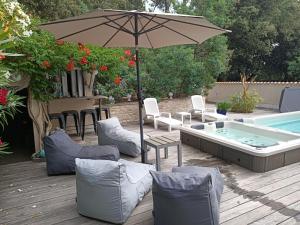 a patio with an umbrella and chairs and a pool at Pomme de Pin et Mimosa in Grand-Village-Plage