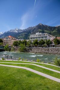 a walkway next to a river with buildings and mountains at Hotel Aurora in Merano