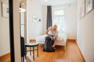 莱比锡Hostel Multitude的一名男子坐在床上,袋子放在地板上