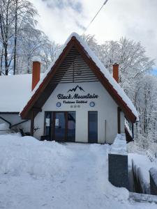 a building with snow on the ground in front of it at Pensiunea Black Mountain in Baia-Sprie