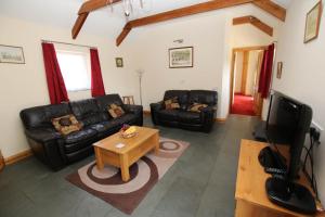a living room with black leather furniture and a flat screen tv at Chy un Lur Rural cottage in Truro