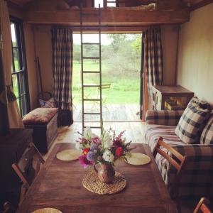 een woonkamer met een tafel met bloemen erop bij Sky View Shepherd's Huts with Woodburning Hot Tub in Redruth