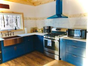 uma cozinha com armários azuis, um fogão e um lavatório em Charming 120-year-old farmhouse by the creek. em Starlight