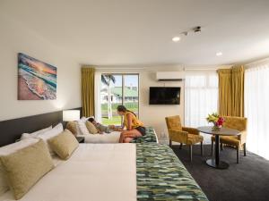 a woman sitting on a bed in a hotel room at Carnmore Hotel Takapuna in Auckland