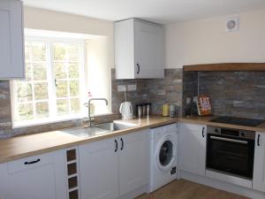 cocina con armarios blancos, fregadero y lavavajillas en Tuckermarsh Quay River Cottage 2 en Bere Alston