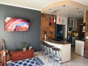 a kitchen with a bar with stools and a tv on the wall at Hacienda Palms in Richards Bay