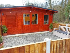 a red cabin with a bench and a fence at The Cabins in Stock