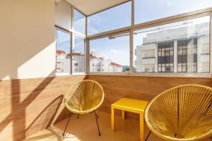 Duas cadeiras e uma mesa amarela num quarto com janelas em RH Charming Apartment - T3 em Barcelos