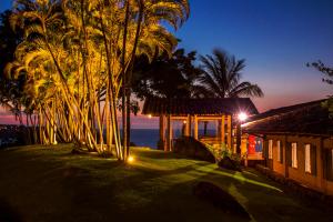 una casa con un patio con palmeras por la noche en Villa Galiileu Ilhabela, en Ilhabela