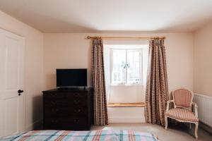 a bedroom with a bed and a tv and a window at Cat and Custard Pot Inn in Shipton Moyne