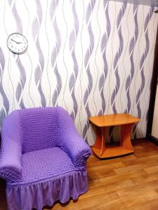 a purple chair next to a table and a clock at Уютные апартаменты c кондиционером на Уманчанке in Umanʼ