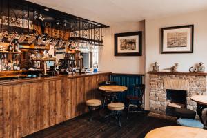 a bar with a fireplace and tables and stools at Cat and Custard Pot Inn in Shipton Moyne