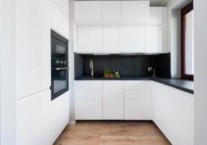 Biała kuchnia z białymi szafkami i czarnymi urządzeniami w obiekcie P&P Apartments w Krakowie