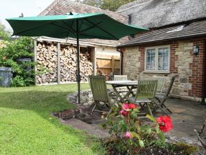 stół i 2 krzesła z zielonym parasolem w obiekcie Forge Cottage w mieście West Lulworth