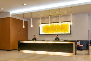 two people sitting at a reception desk in a lobby at Hotel Kanazawa in Kanazawa