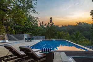 a swimming pool with two chairs and a table next to it at SaffronStays Vedika - 4BR riverfront pool villa with kaya king bullock ride & BBQ near Pinjal River, Vikramgad in Pālghar
