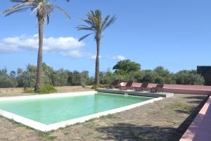 a swimming pool with two chairs and two palm trees at Agriturismo Zinedi in Pantelleria
