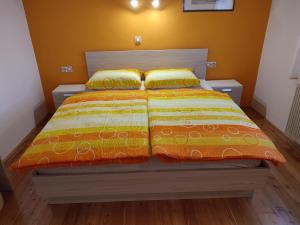 a bed with an orange and yellow comforter and two pillows at Gostilna Pension Blegoš in Poljane nad Škofjo Loko