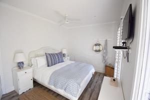a white bedroom with a bed and a tv at Tides' Song in Agulhas
