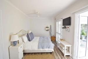 een witte slaapkamer met een bed en een televisie bij Tides' Song in Agulhas