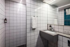 a white tiled bathroom with a sink and a mirror at Comwell H C Andersen Dolce by Wyndham in Odense