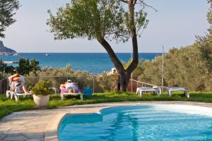 a pool with people sitting in chairs by the ocean at Del Sol Skopelos in Skopelos Town