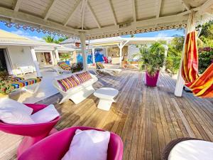 eine Terrasse mit Stühlen und Tischen auf einer Holzterrasse in der Unterkunft Villa Marie, swimming pool, beach, pontoon and jacuzzi, all private in Baie Nettle