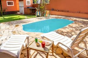 a swimming pool with two chairs and a table with drinks at Casa com piscina a 350m da praia em Boiçucanga in Boicucanga