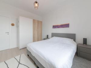 ein weißes Schlafzimmer mit einem weißen Bett und einem Nachttisch in der Unterkunft Apartment Carnac Station by Interhome in De Haan