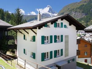 a white building with green shutters and a mountain at Apartment Hubertus-2 by Interhome in Zermatt