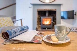 a table with a book and a cup of coffee and a newspaper at 2 Riverside Cottages in Saxmundham