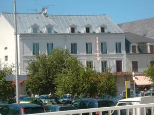 Un gran edificio blanco con coches aparcados en un estacionamiento. en Hotel De La Gare, en Montluçon