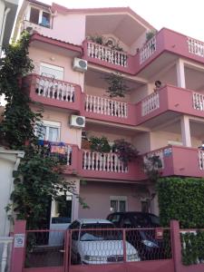 un edificio rosa con balcones y coches aparcados delante en Rooms Kuljic, en Budva