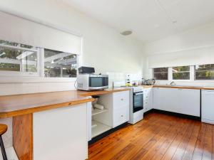a white kitchen with wooden floors and white cabinets at Myall River Cottage in Tea Gardens