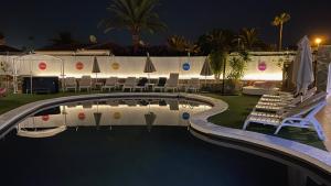 a swimming pool at night with chairs and umbrellas at Rainbow Golf Bungalows, Gay Men-only Resort in Maspalomas