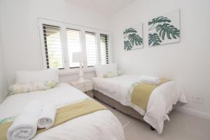 1002 Bermudas - by Stay in Umhlanga في ديربان: سريرين في غرفة نوم بجدران بيضاء ونوافذ
