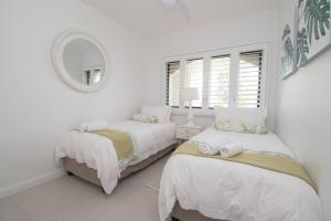 1002 Bermudas - by Stay in Umhlanga في ديربان: غرفة نوم بيضاء بسريرين ومرآة