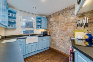 a kitchen with blue cabinets and a stone wall at Penlee Narrows - Kingsand in Kingsand