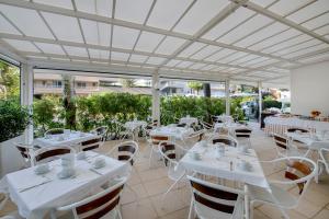 a restaurant with white tables and chairs and windows at Hotel Sanremo in Milano Marittima