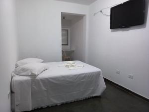 a white bedroom with a bed and a flat screen tv at PLANALTO HOTEL II in Arujá +1 photo